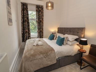A bedroom with a bed with pillows and towels by a window with patterned curtains at The Furness Haven in Barrow-In-Furness