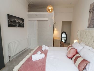 A bedroom with a bed towels pillows a desk a hanging light and a wall mirror at The Furness Haven in Barrow-In-Furness