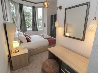 A bedroom with a bed, bedside table with lamp, wardrobe, vanity table with mirror and stool at The Furness Haven in Barrow-In-Furness