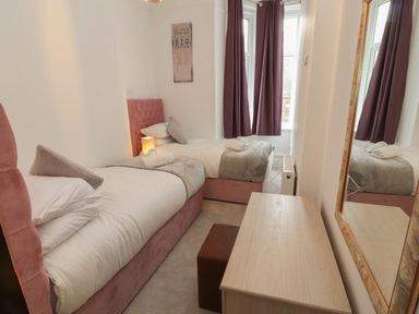 A bedroom with two single beds a wooden desk a square stool and a wall mirror at The Furness Haven in Barrow-In-Furness
