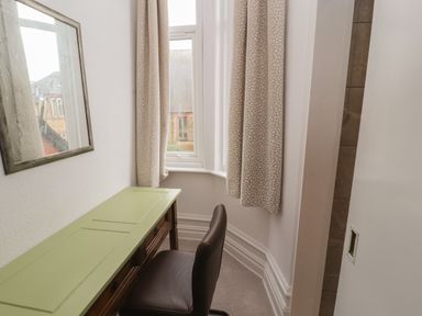 A small room with a green desk a brown chair a window with curtains and a wall mirror at The Furness Haven in Barrow-In-Furness