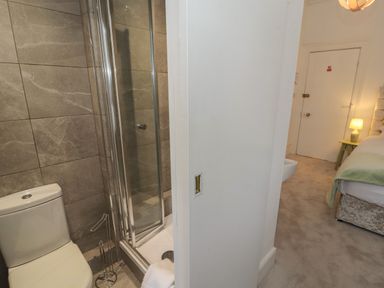 A bathroom with a toilet and shower next to a bedroom with a bed lamp and side table at The Furness Haven in Barrow-In-Furness