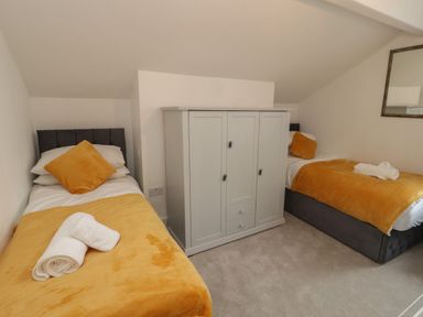 A bedroom with two single beds with yellow blankets a white cabinet between beds and a mirror on the wall at The Furness Haven in Barrow-In-Furness
