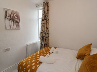 A bedroom with a bed covered with white and patterned orange bedding by a window with patterned curtains at The Furness Haven in Barrow-In-Furness