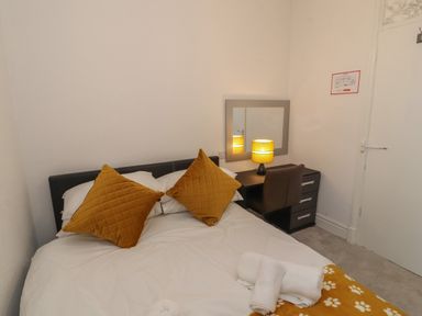 A bedroom with a bed with mustard pillows a desk with a lamp and chair and towels on the bed at The Furness Haven in Barrow-In-Furness