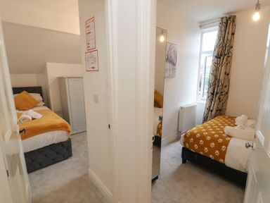 Two small bedrooms with single beds and yellow blankets separated by a wall at The Furness Haven in Barrow-In-Furness