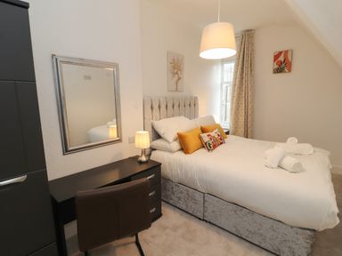 A bedroom with a bed with pillows and towels beside a desk with a chair and a lamp at The Furness Haven in Barrow-In-Furness