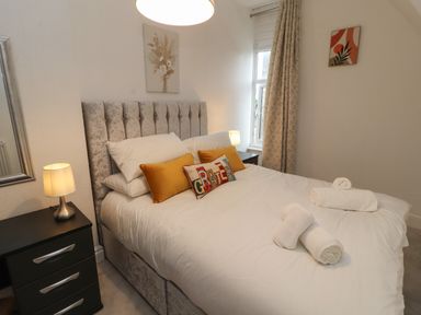 A bedroom with a bed featuring white bedding and decorative pillows beside a window with curtains and nightstands with lamps at The Furness Haven in Barrow-In-Furness