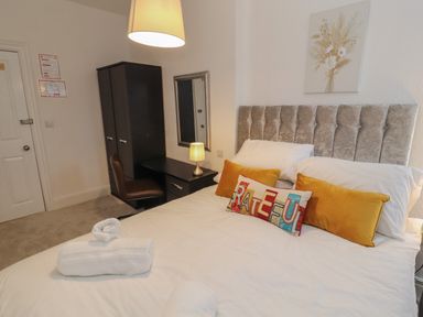 A bedroom with a bed with pillows and folded towels a desk with a lamp a chair a mirror and a wardrobe at The Furness Haven in Barrow-In-Furness