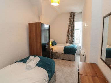 A bedroom with two single beds a wardrobe a dresser and a window with curtains at The Furness Haven in Barrow-In-Furness