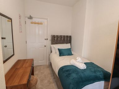 A small bedroom with a single bed, wooden dresser, mirror, and a door at The Furness Haven in Barrow-In-Furness