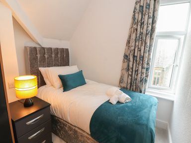 A bedroom with a single bed a nightstand with a lamp and a window with patterned curtains at The Furness Haven in Barrow-In-Furness