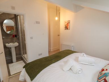 A bedroom with a bed, folded towels on the bed, a radiator, a bathroom with a sink and shower visible at The Furness Haven in Barrow-In-Furness