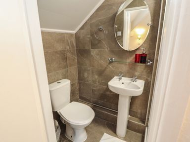 A bathroom with a toilet pedestal sink round mirror and soap dispensers at The Furness Haven in Barrow-In-Furness