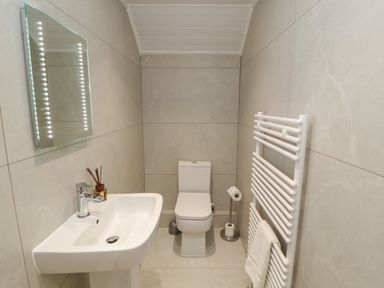 A small bathroom with a toilet, a sink, an illuminated mirror, and a towel radiator at The Furness Haven in Barrow-In-Furness