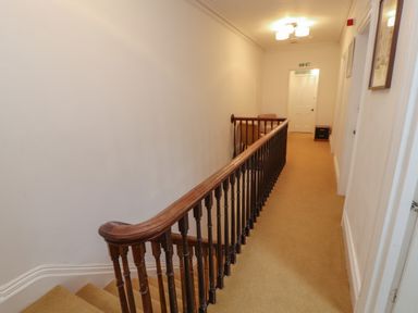A carpeted hallway with wooden stair railing and closed doors at The Furness Haven in Barrow-In-Furness