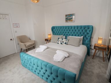 A bedroom with a turquoise upholstered bed and two bedside tables with lamps at The Furness Haven in Barrow-In-Furness
