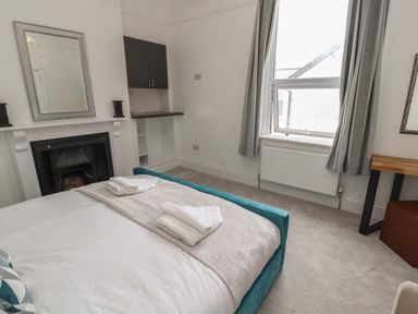 A bedroom with a bed towels on bed a fireplace a window with curtains and a small desk at The Furness Haven in Barrow-In-Furness
