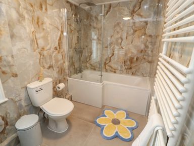 A bathroom with a toilet a bathtub with shower and a flower shaped rug at The Furness Haven in Barrow-In-Furness