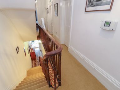 A carpeted staircase with wooden railing and a hallway with doors and framed pictures at The Furness Haven in Barrow-In-Furness