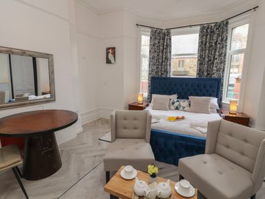 A bedroom with a blue bed, two beige chairs, a wooden round table, and a small wooden coffee table with teapots at The Furness Haven in Barrow-In-Furness