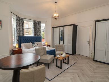A bedroom with a blue bed headboard two armchairs small tables two wardrobes and a round dining table at The Furness Haven in Barrow-In-Furness