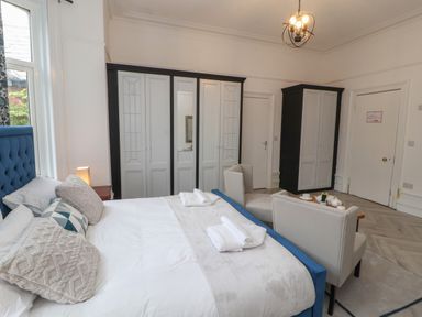 A bedroom with a large bed pillows wardrobes a small table with chairs and a window at The Furness Haven in Barrow-In-Furness