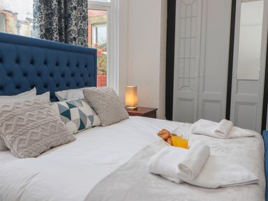 A bedroom with a blue upholstered headboard a bed with pillows towels croissants and orange juice at The Furness Haven in Barrow-In-Furness