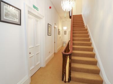 A carpeted staircase with wooden railing in a hallway with white doors and framed pictures at The Furness Haven in Barrow-In-Furness