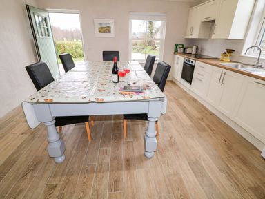 A kitchen with a dining table covered with a plastic tablecloth and six chairs next to cabinets and a stove at The Poets Cottage in Portglenone