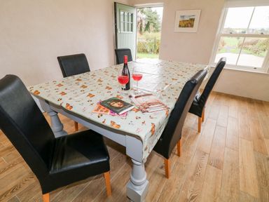 A dining room with a table, four black chairs, a bottle and two glasses of red drink, three books on the table and a door and window showing outside at The Poets Cottage in Portglenone
