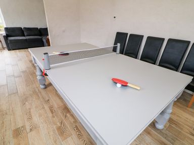 A room with a table tennis table and paddles with chairs along the wall and a black sofa in the corner at The Poets Cottage in Portglenone