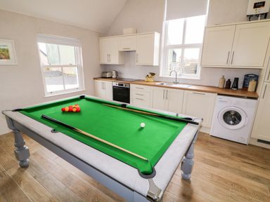 A kitchen with white cabinets and wooden countertops and a snooker table in the center at The Poets Cottage in Portglenone