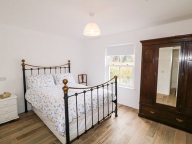 A bedroom with a metal bed frame floral bedding a wooden wardrobe with mirror and a small bedside table at The Poets Cottage in Portglenone