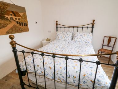 A bedroom with a metal bed frame floral bedding a wooden chair and a woven wall hanging at The Poets Cottage in Portglenone
