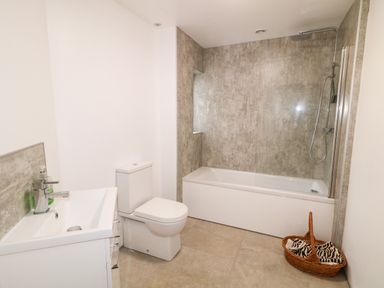 A bathroom with a sink and faucet toilet bathtub with shower and basket with towels at The Poets Cottage in Portglenone