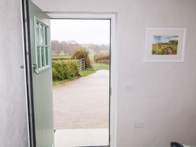 An open green door showing a view of a driveway and countryside with a framed picture on a white wall at The Poets Cottage in Portglenone