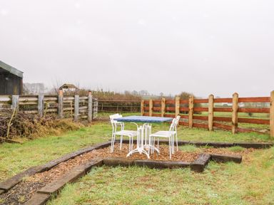 An outdoor seating area with a table and four chairs on a wood chip ground surrounded by a wooden fence at The Poets Cottage in Portglenone