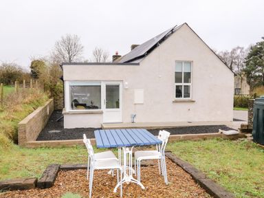A white house with solar panels and a blue table with white chairs outside at The Poets Cottage in Portglenone