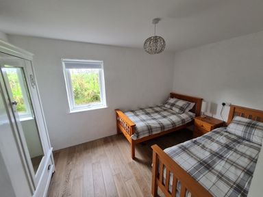 A bedroom with two single wooden beds a wooden nightstand with a lamp a window and a white wardrobe at The Poets Cottage in Portglenone