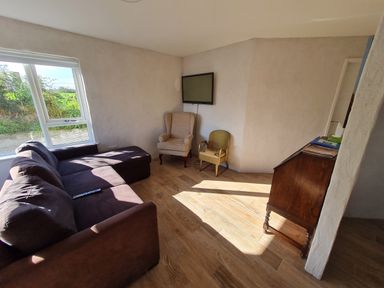 A living room with a sectional sofa two chairs a wall-mounted television and a wooden cabinet at The Poets Cottage in Portglenone