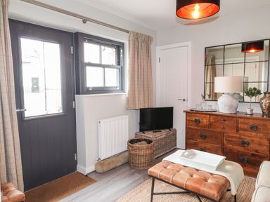 A living room with a dark door and window curtains a wooden dresser with a lamp and mirror and a leather bench at The Pottery in Newport Pembrokeshire