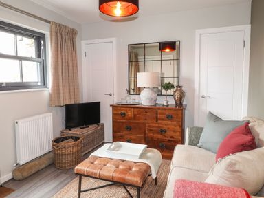 A living room with a sofa cushions leather ottoman wooden dresser and a small TV at The Pottery in Newport Pembrokeshire