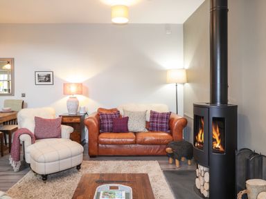 A living room with a leather sofa an armchair wood burning stove and wooden coffee table at The Pottery in Newport Pembrokeshire
