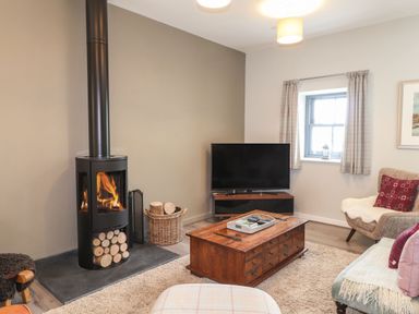 A living room with a wood-burning stove TV wooden coffee table and armchairs at The Pottery in Newport Pembrokeshire