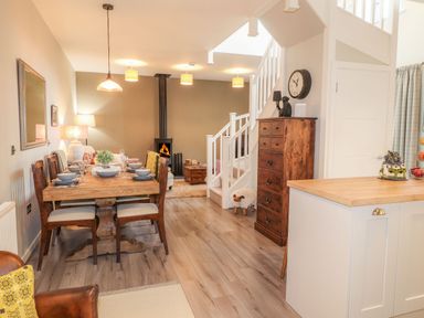 A dining area with a wooden table set with dishes and chairs next to a living room with a fireplace and stairs at The Pottery in Newport Pembrokeshire