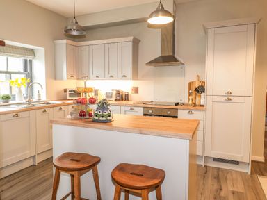 A kitchen with wooden stools a kitchen island fruit basket and white cabinets at The Pottery in Newport Pembrokeshire