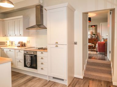 A kitchen with white cabinets wooden countertops and stainless steel appliances with a view into a living room at The Pottery in Newport Pembrokeshire