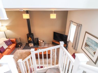 A living room with a leather sofa a wood stove and a television viewed from a staircase at The Pottery in Newport Pembrokeshire