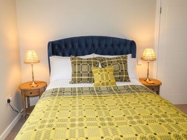 A bedroom with a blue upholstered headboard a bed with yellow patterned bedding and two wooden bedside tables with lamps at The Pottery in Newport Pembrokeshire
